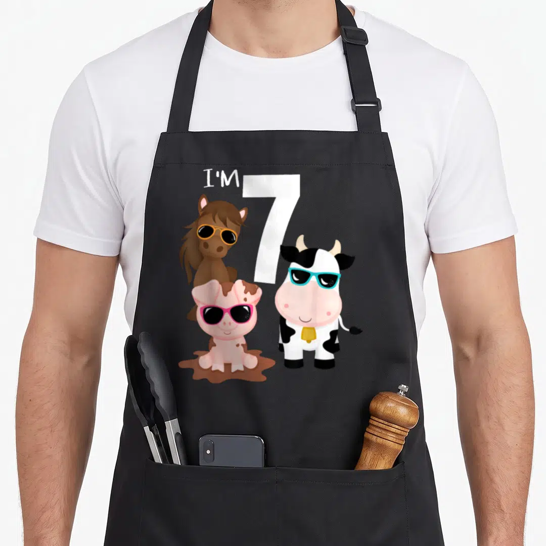 7th farm apron - Cartoon horse cow and pig wearing sunglasses next to I'M 7 text — shown on a black cotton canvas apron against a white background