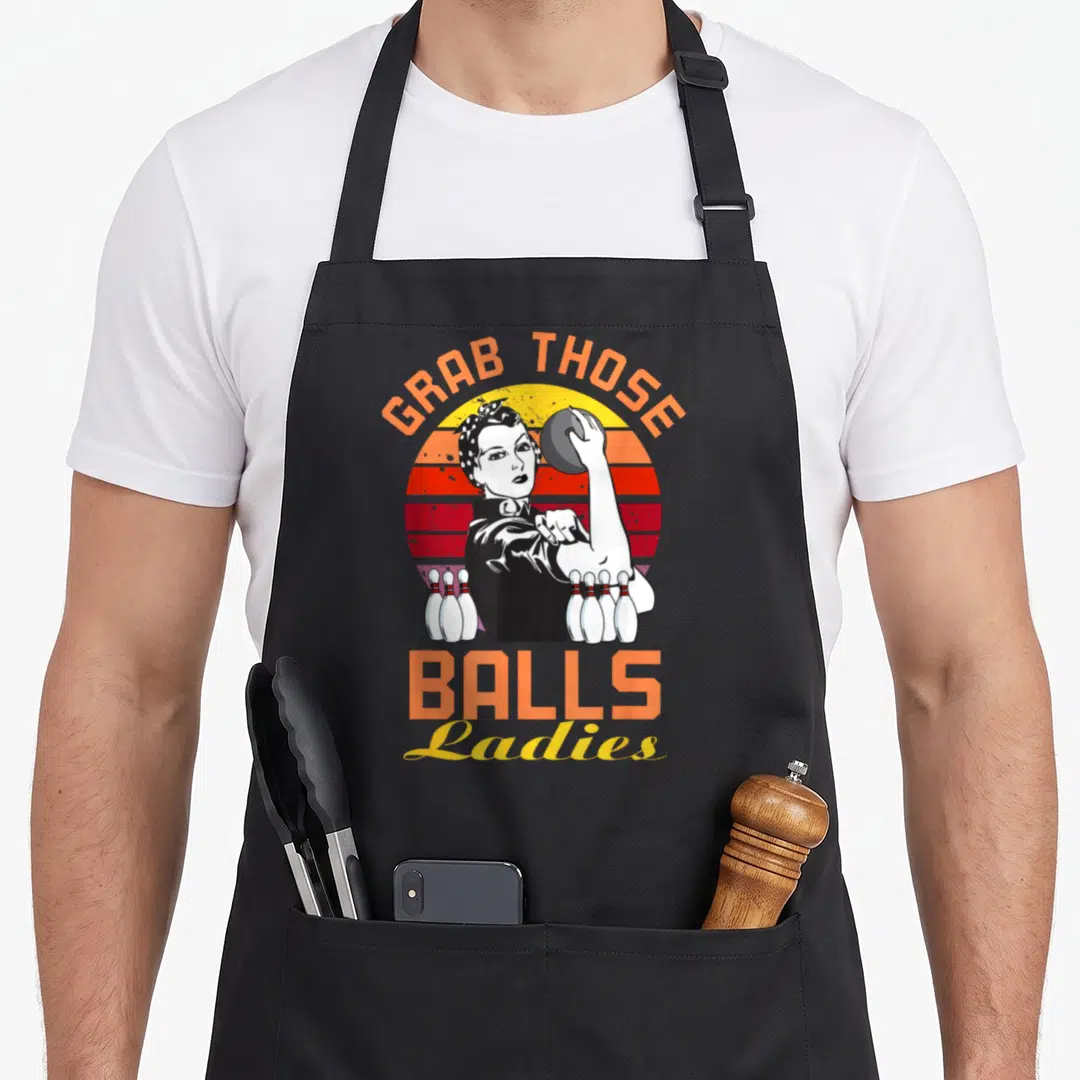 Grab novelty apron - Retro woman holding bowling ball with GRAB THOSE BALLS Ladies text and pins — shown on a black cotton canvas apron against a white background