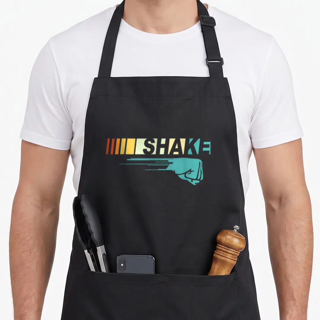 Shake family aprons - Teal fist with motion lines below SHAKE text and vertical colored stripes — shown on a black cotton canvas apron against a white background