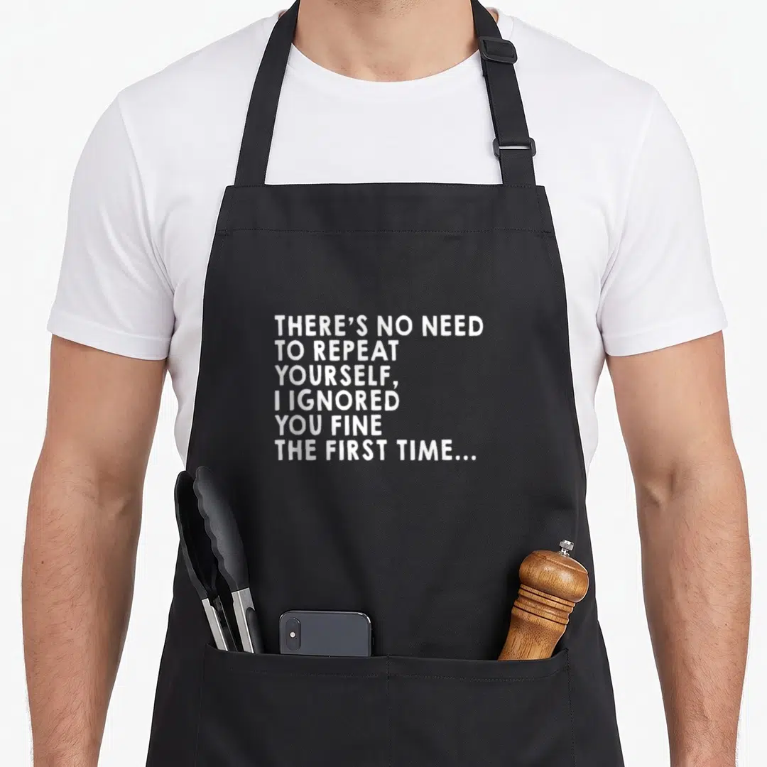 Repeat sarcastic apron - White stacked text reading There's No Need To Repeat Yourself I Ignored You Fine The First Time — shown on a black cotton canvas apron against a white background
