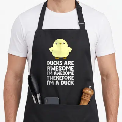 Therefore duck apron - Yellow cartoon duck above stacked white text reading Ducks Are Awesome I'm Awesome Therefore I'm — shown on a black cotton canvas apron against a white background