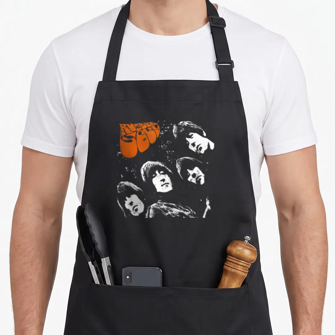 Soul rubber apron - RUBBER SOUL text and four white faces in distressed orange and white print — shown on a black cotton canvas apron against a white background