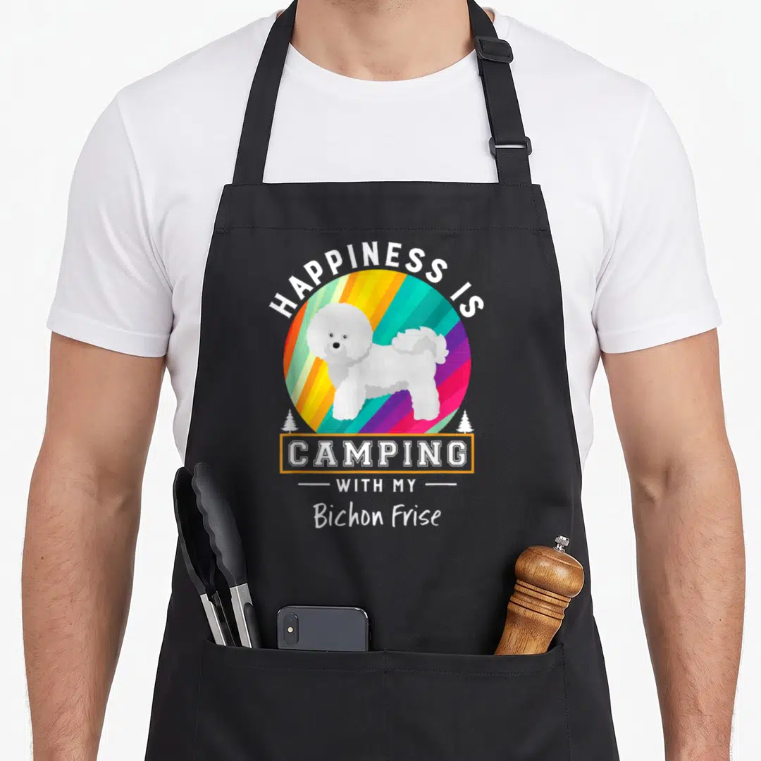 Outdoor dog apron - White Bichon Frise standing in front of a rainbow striped circle with camping text — shown on a black cotton canvas apron against a white background