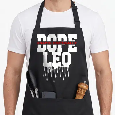 Astrology king apron - Stacked white DOPE and LEO text with red UNAPOLOGETICALLY overlay and dripping paint effect — shown on a black cotton canvas apron against a white background