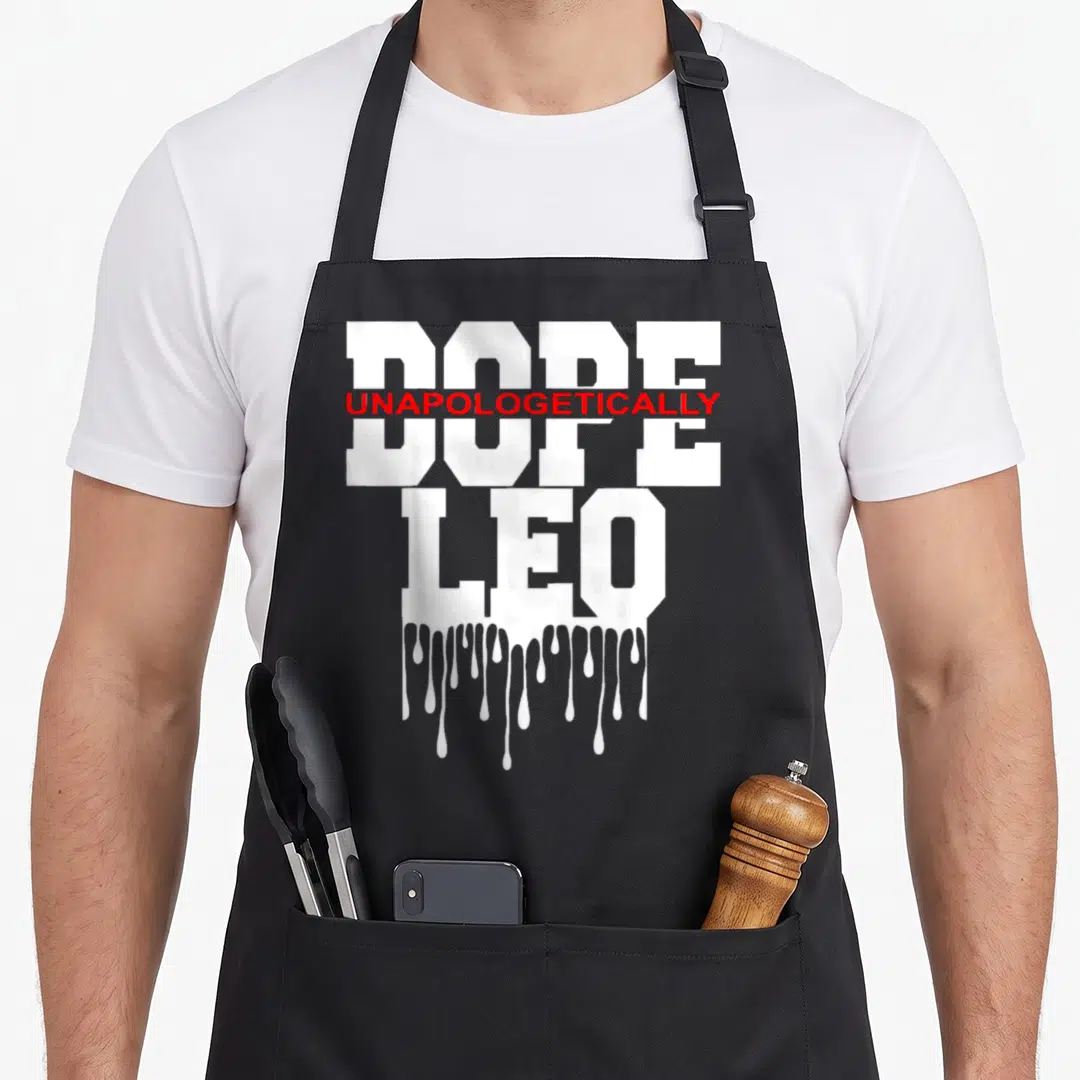 Astrology king apron - Stacked white DOPE and LEO text with red UNAPOLOGETICALLY overlay and dripping paint effect — shown on a black cotton canvas apron against a white background