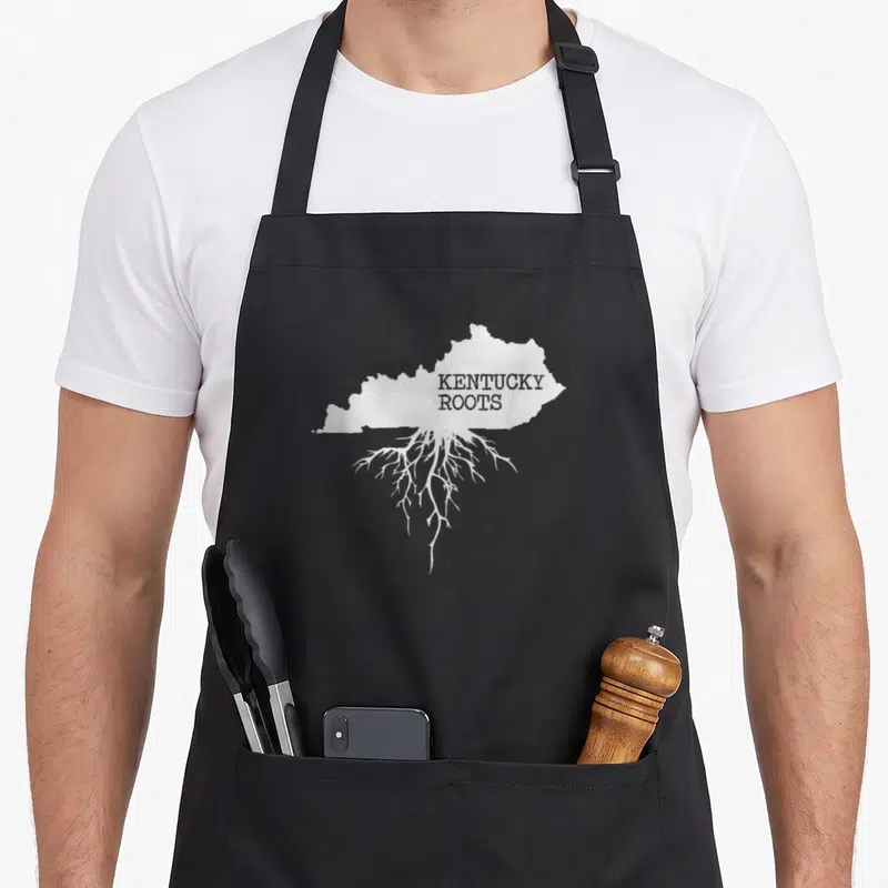 Root kentucky apron - White Kentucky map silhouette with downward roots and grey text on black fabric — shown on a black cotton canvas apron against a white background