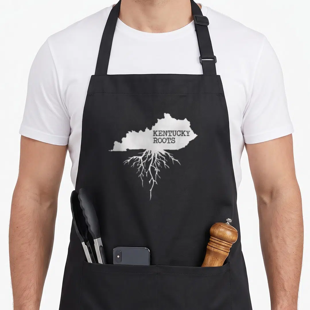 Root kentucky apron - White Kentucky map silhouette with downward roots and grey text on black fabric — shown on a black cotton canvas apron against a white background
