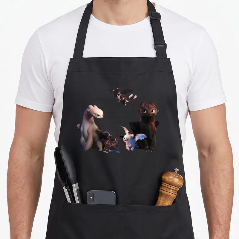 Train family aprons - Four cartoon dragons in black, white, and grey clustered together — shown on a black cotton canvas apron against a white background