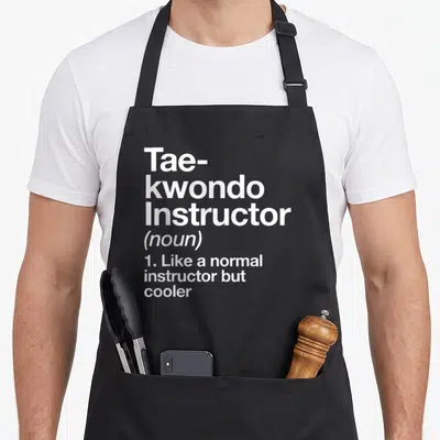 Instructor martial apron - White stacked text reading Tae-kwondo Instructor noun like normal but cooler — shown on a black cotton canvas apron against a white background