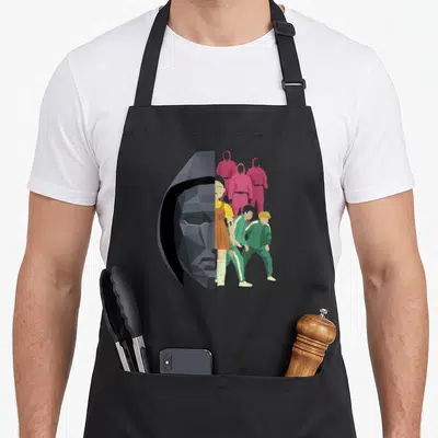 Cute split apron - Grey geometric mask split with pink and green jumpsuit figures and orange dress detail — shown on a black cotton canvas apron against a white background