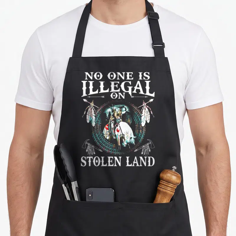Illegal stolen native american apron - Distressed rider on horseback flanked by spears and tomahawks with white text NO — shown on a black cotton canvas apron against a white background