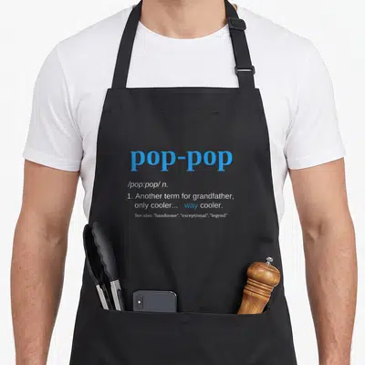 Pop father day apron - Blue and white text defining pop-pop as a grandfather term that is way cooler — shown on a black cotton canvas apron against a white background