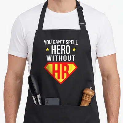 Human super hero aprons - Stacked white text YOU CAN T SPELL HERO WITHOUT HR with two yellow stars and red yellow — shown on a black cotton canvas apron against a white background