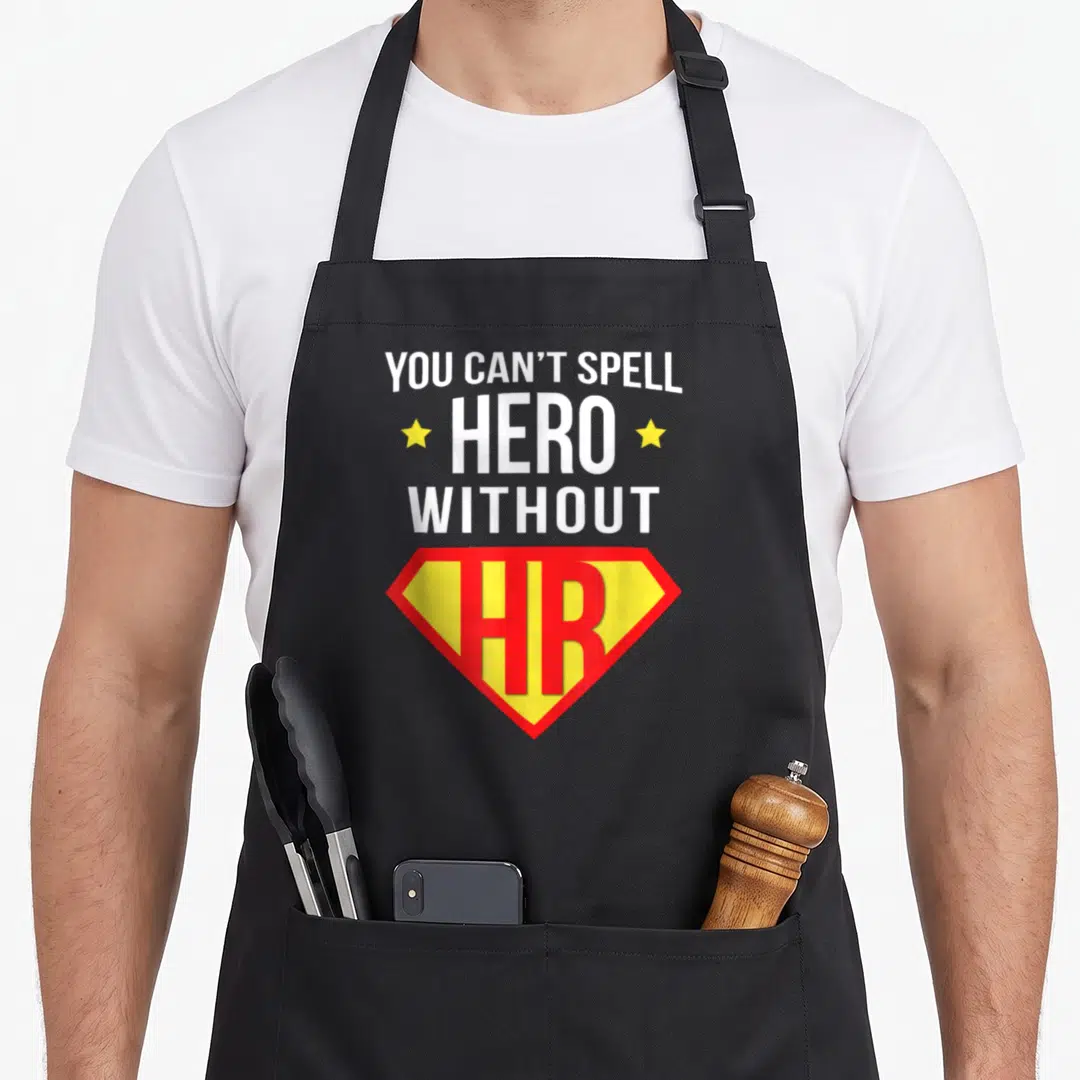 Human super hero aprons - Stacked white text YOU CAN T SPELL HERO WITHOUT HR with two yellow stars and red yellow — shown on a black cotton canvas apron against a white background