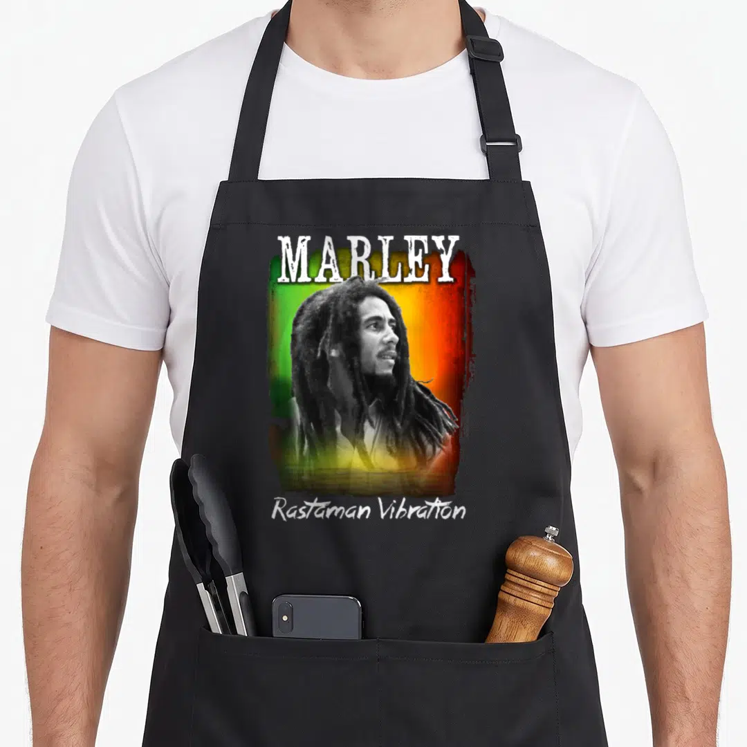 Marley reggae apron - Realistic Bob Marley portrait with MARLEY and Rastaman Vibration text over green yellow red — shown on a black cotton canvas apron against a white background