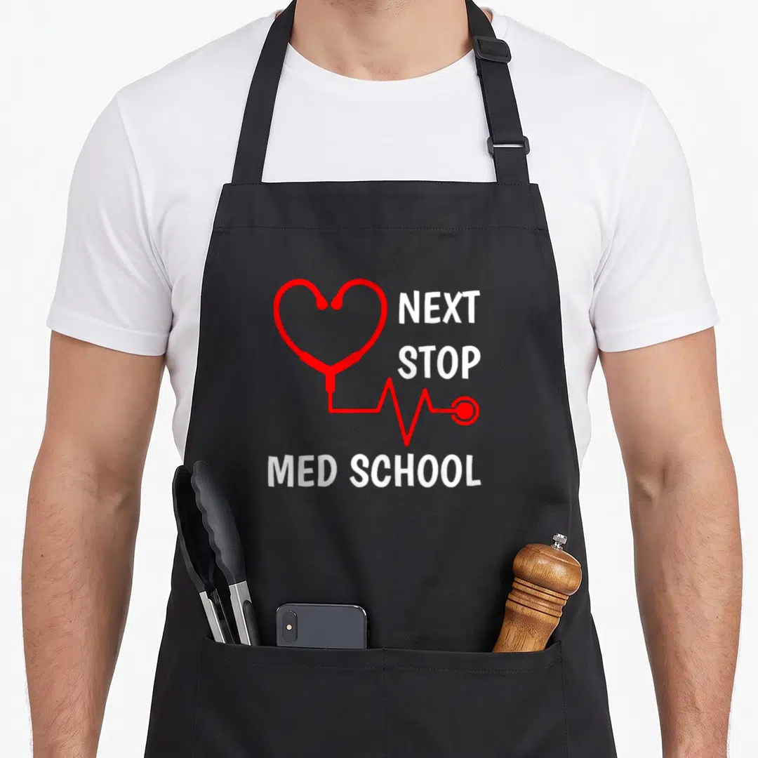 Stop student aprons - Red stethoscope heart shape with NEXT STOP MED SCHOOL text in white — shown on a black cotton canvas apron against a white background