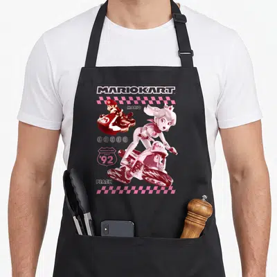 Racing princess apron - Retro print of Mario and Peach on karts with pink checkered borders and Since 92 text — shown on a black cotton canvas apron against a white background