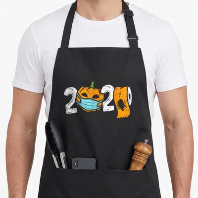 Mask halloween kitchen aprons - 2020 text with masked pumpkin and toilet paper roll in orange white and blue — shown on a black cotton canvas apron against a white background