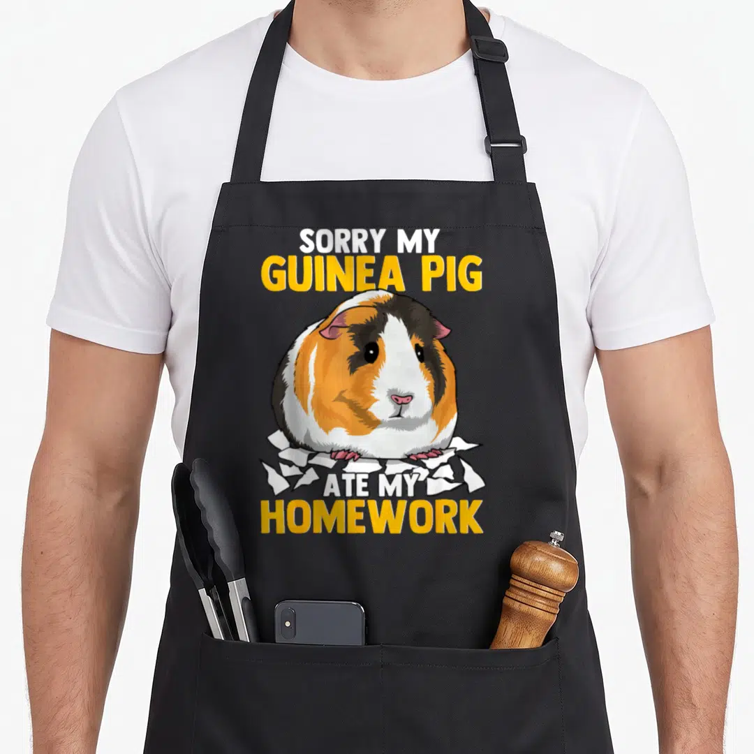 Sorry pet apron - Cartoon guinea pig sitting on torn paper with yellow and white text SORRY MY GUINEA PIG ATE MY — shown on a black cotton canvas apron against a white background