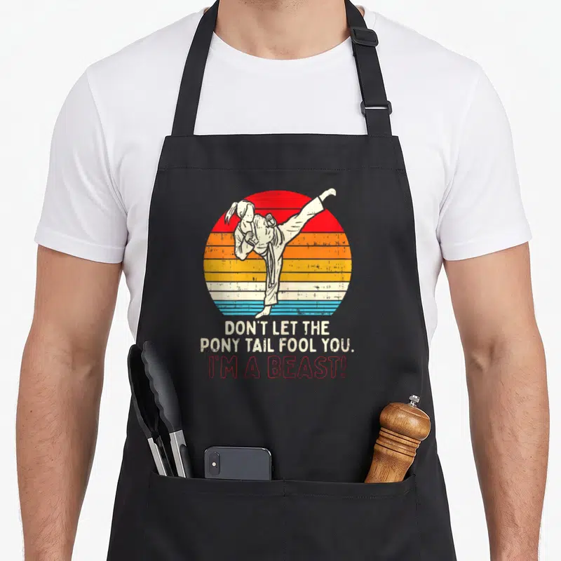 Boredkoalas x apron - Retro martial artist high kick against striped sun with beast text — shown on a black cotton canvas apron against a white background