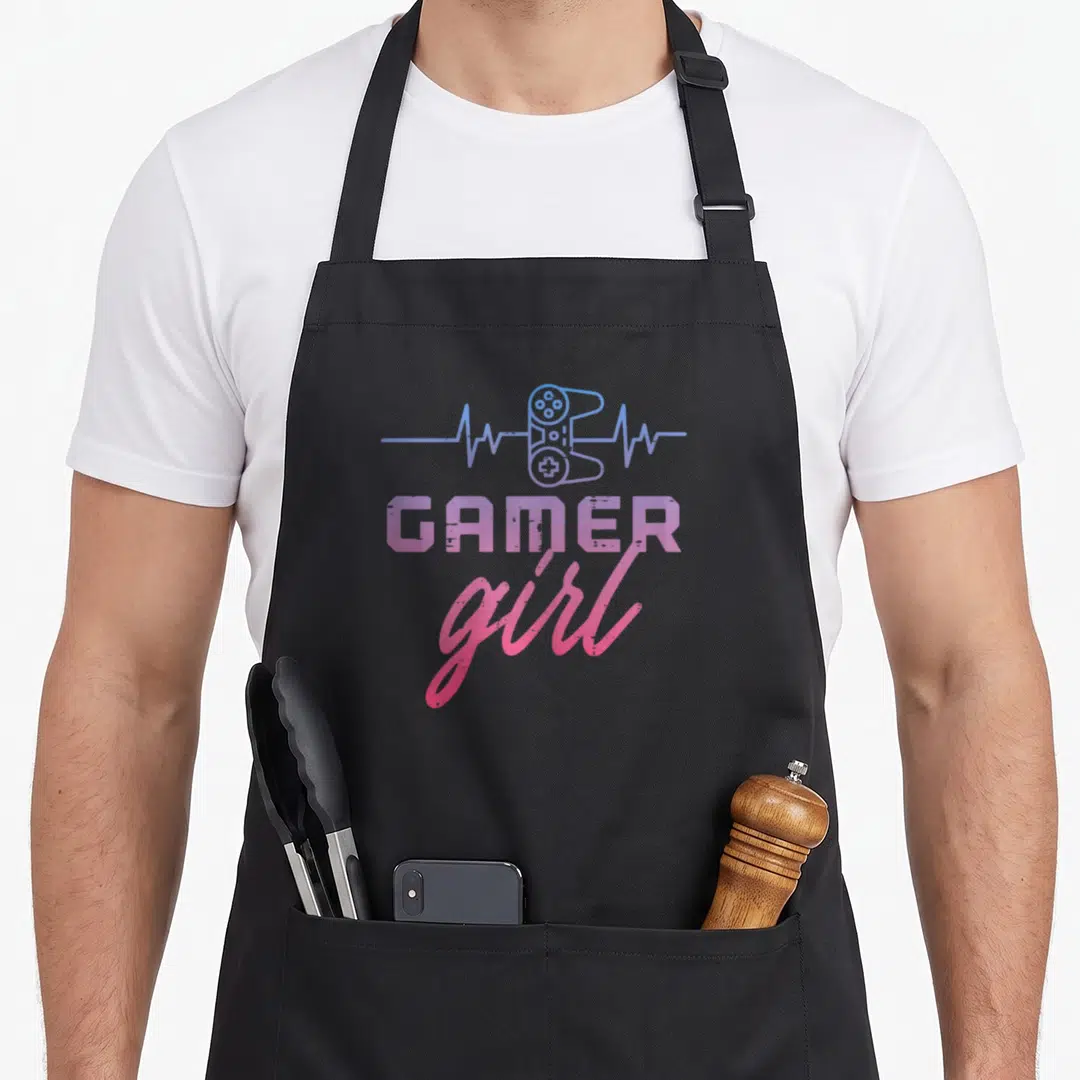 Youth gaming apron - Blue and pink gradient game controller inside a heartbeat line above stacked GAMER girl text — shown on a black cotton canvas apron against a white background
