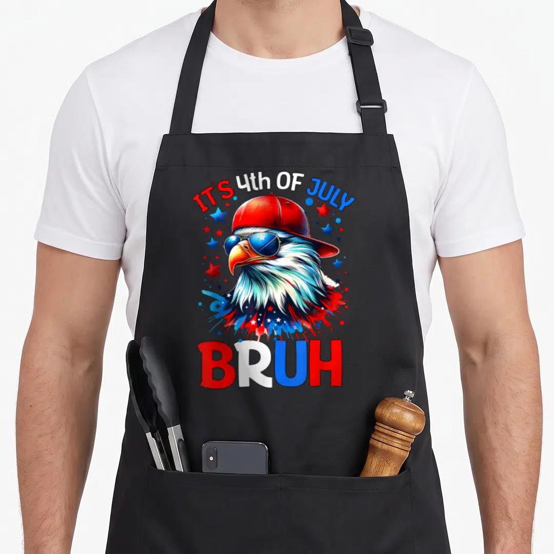 Bruh 4th of july apron - Cartoon bald eagle in red cap and blue sunglasses with IT'S 4th OF JULY BRUH text — shown on a black cotton canvas apron against a white background
