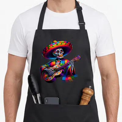 Cinco skeleton apron - Cartoon skeleton in rainbow sombrero and poncho playing decorated guitar — shown on a black cotton canvas apron against a white background