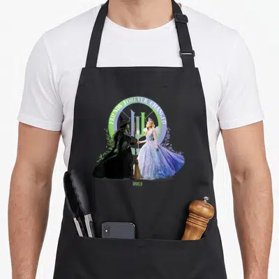 Wicked friends apron - Two witches holding broom and wand under arched text FRIENDS FOREVER CHANGED on green purple — shown on a black cotton canvas apron against a white background