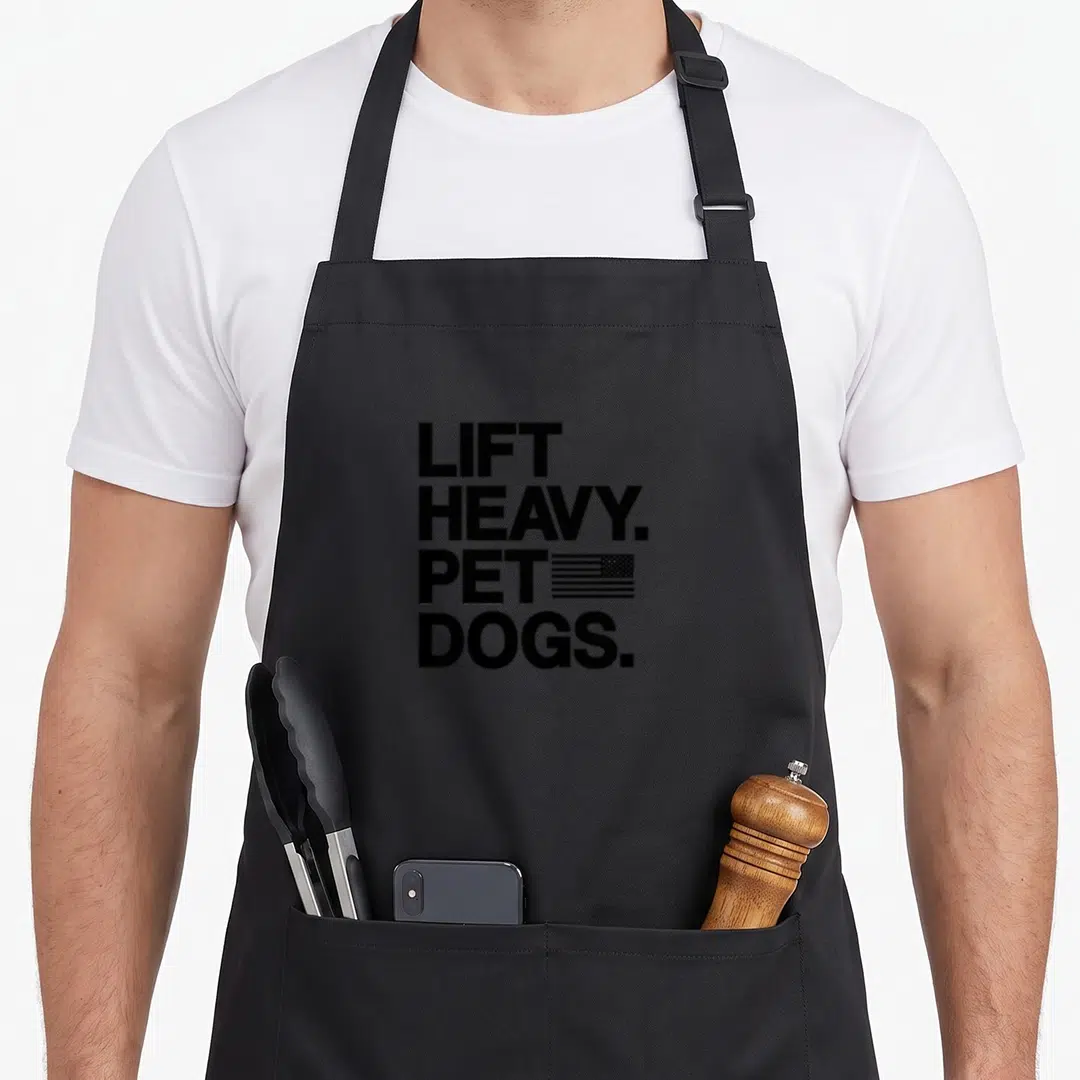 Lift heavy dog apron - Black LIFT HEAVY PET DOGS text with small US flag graphic — shown on a black cotton canvas apron against a white background