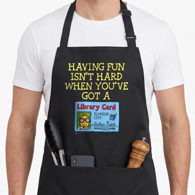 Arthur card apron - Yellow text above blue library card with aardvark photo and Arthur Read signature — shown on a black cotton canvas apron against a white background