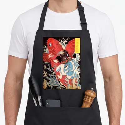 Artwork fish apron - Man wrestling large red fish in blue waves with yellow text box, vintage Japanese style — shown on a black cotton canvas apron against a white background