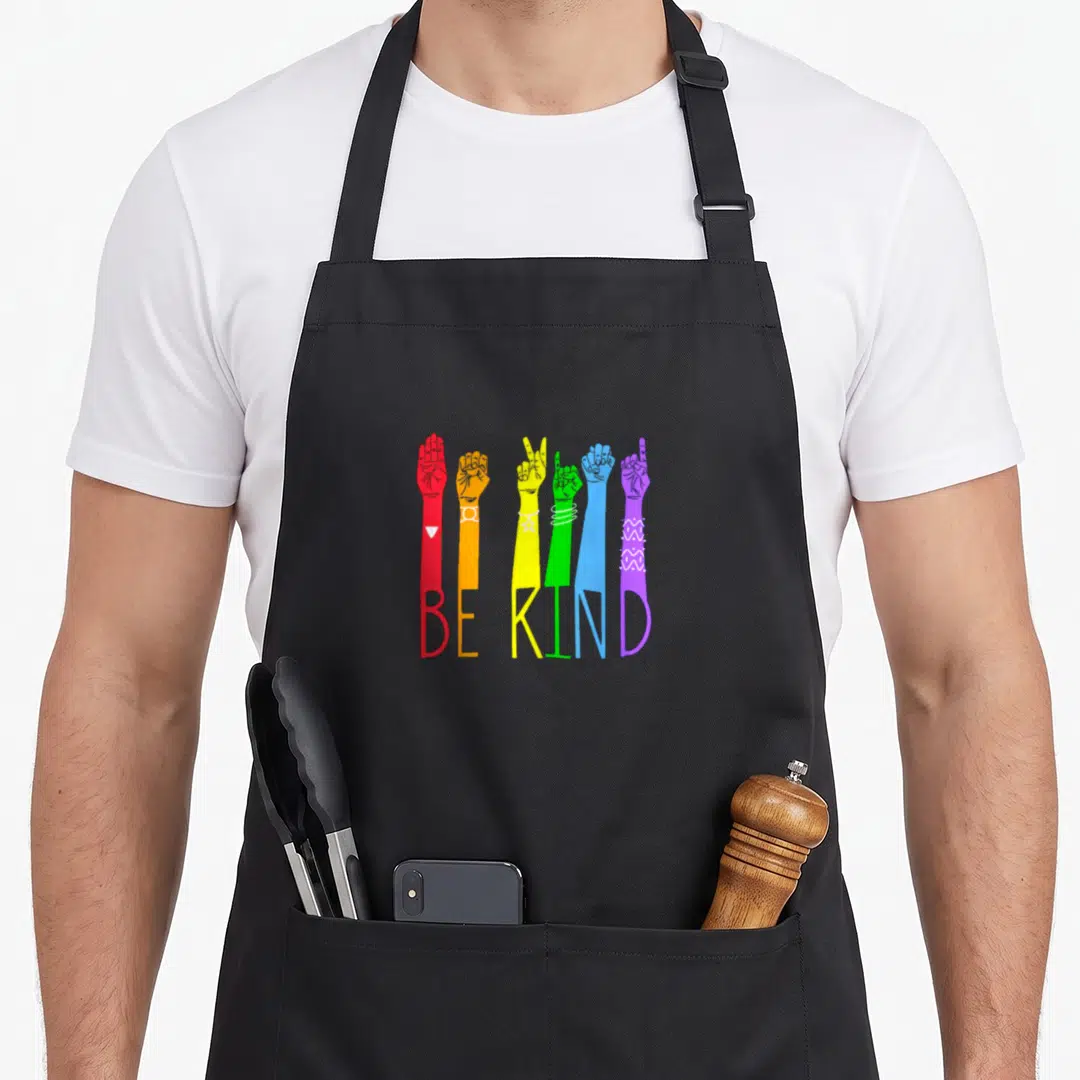 Talking asl sign for apron - Six rainbow arms forming BE KIND letters with hand signs in cartoon style — shown on a black cotton canvas apron against a white background