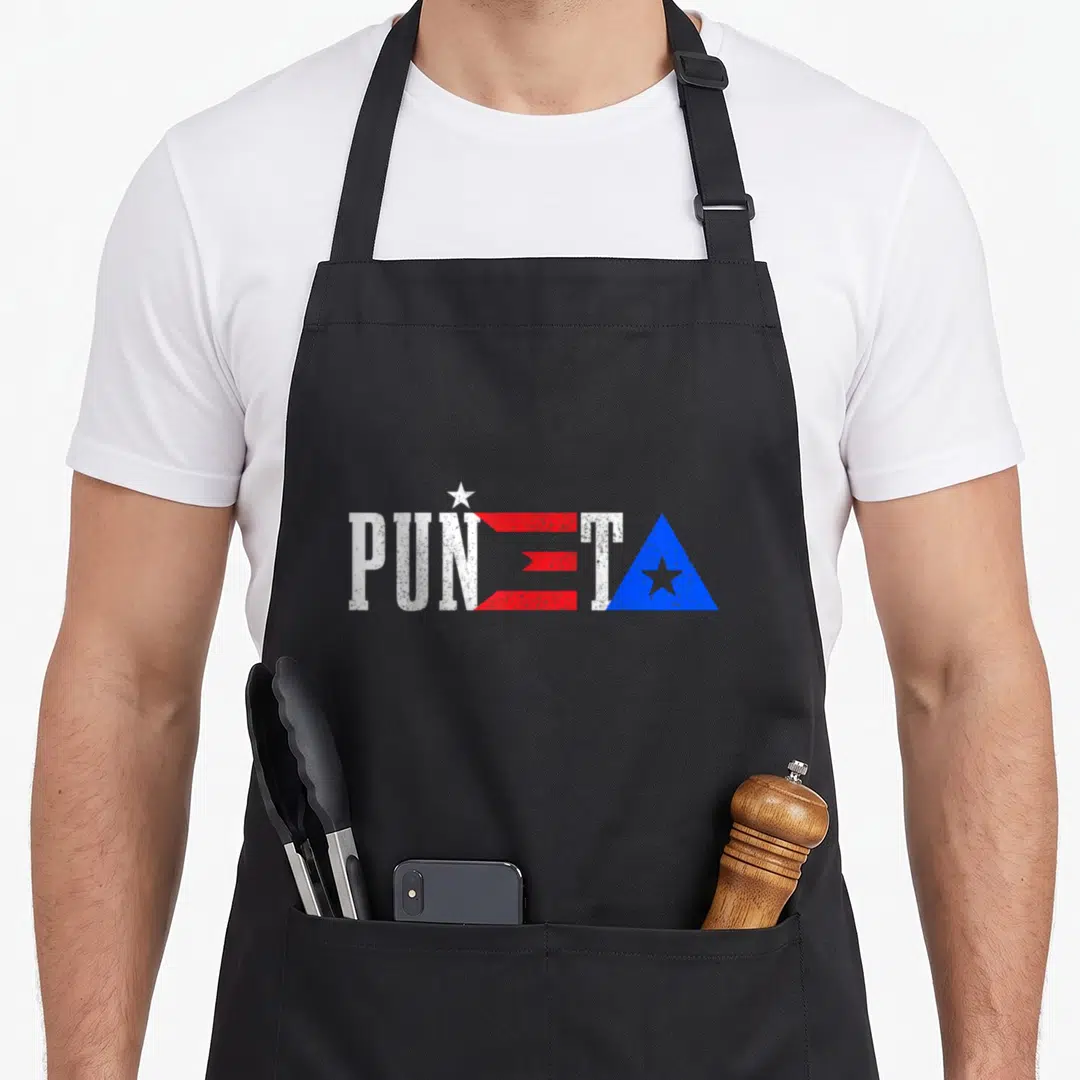 Eta pride apron - PUÑETA text filled with Puerto Rican flag colors white red and blue star triangle — shown on a black cotton canvas apron against a white background