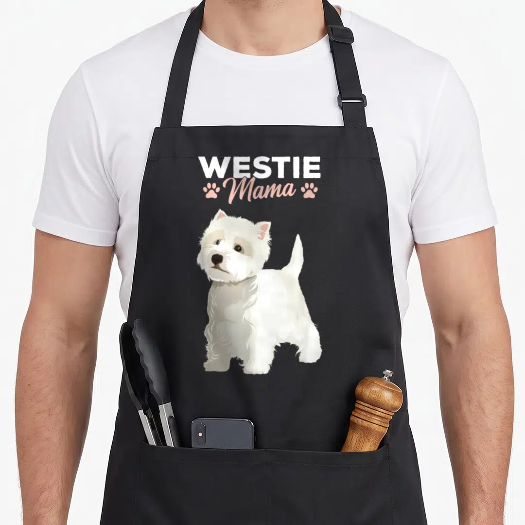 Mama westie apron - White West Highland Terrier standing below WESTIE Mama text flanked by pink paw prints — shown on a black cotton canvas apron against a white background