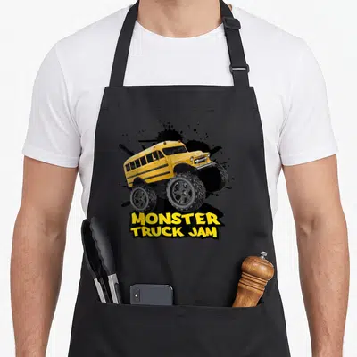 Bus truck apron - Yellow monster truck school bus over black splatter with stacked text — shown on a black cotton canvas apron against a white background