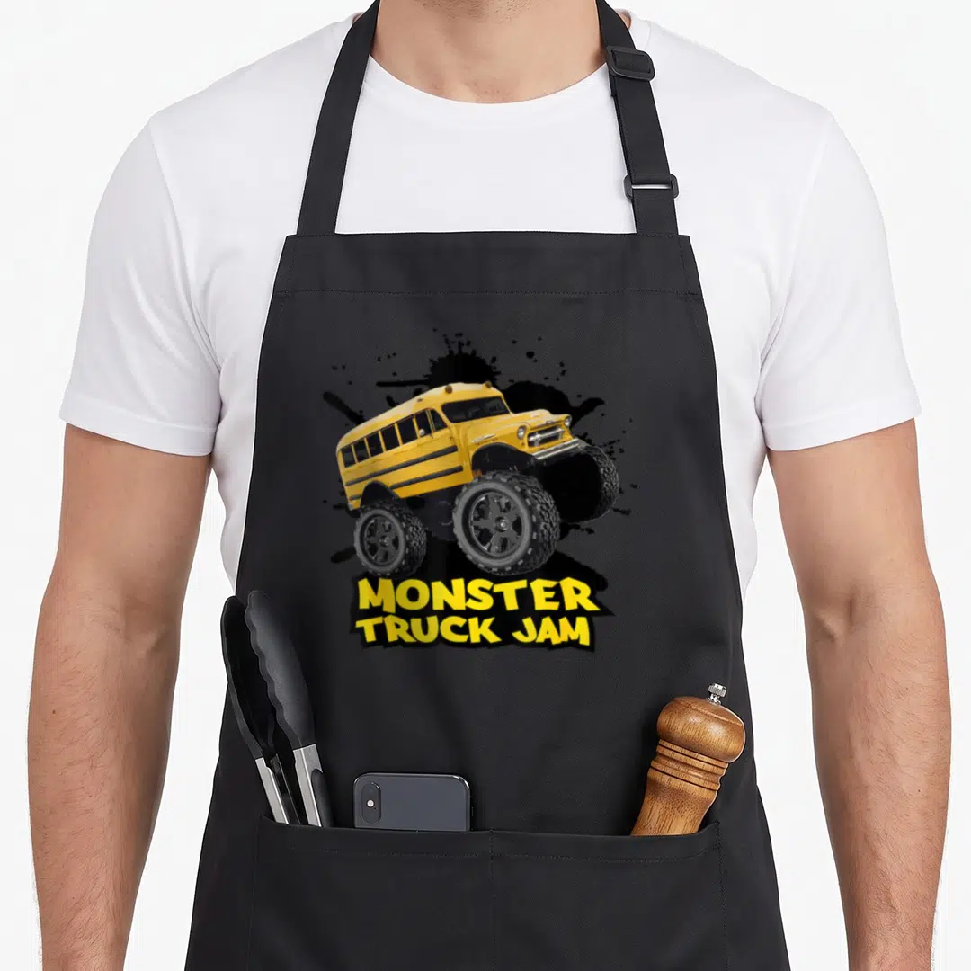 Bus truck apron - Yellow monster truck school bus over black splatter with stacked text — shown on a black cotton canvas apron against a white background