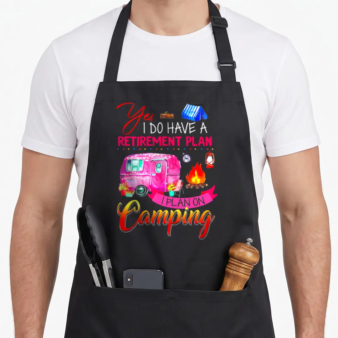 Plan camping apron - Camper van, campfire, and text Yes I Do Have A Retirement Plan in pink and blue — shown on a black cotton canvas apron against a white background