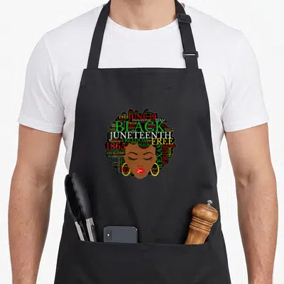 Juneteenth melanin hair apron - Woman's face with Afro composed of Juneteenth, Freedom, 1865, and Emancipation words — shown on a black cotton canvas apron against a white background