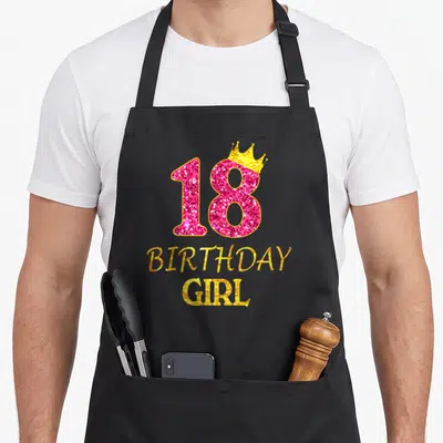 18th princess apron - Glittery pink 18 with gold crown and stacked BIRTHDAY GIRL text — shown on a black cotton canvas apron against a white background