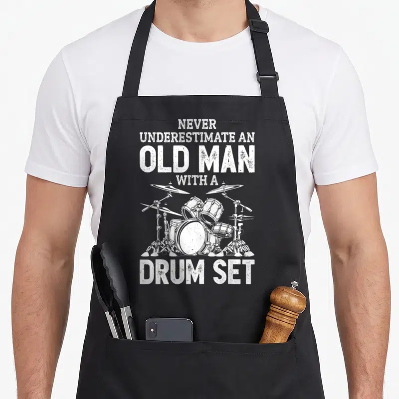 Drummer papa pigeon apron - Distressed white text and drum kit illustration on grey background — shown on a black cotton canvas apron against a white background