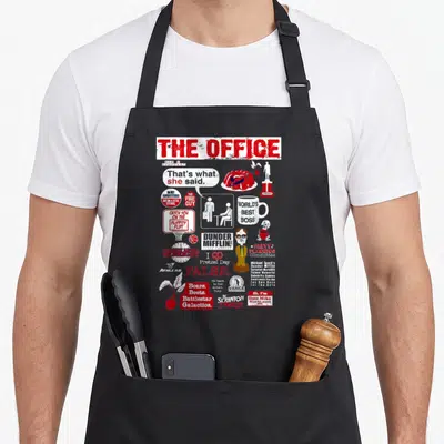 Retro food novelty apron - The Office quote collage with That's what she said and Bears Beets Battlestar Galactica text — shown on a black cotton canvas apron against a white background