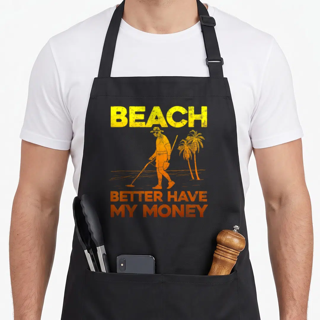 Beach metal detecting apron - Distressed yellow and orange graphic of metal detectorist scanning sand with palm trees — shown on a black cotton canvas apron against a white background