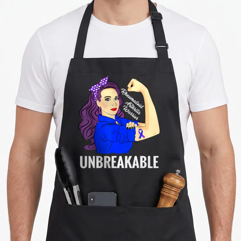 Warrior rheumatoid arthritis awareness apron - Cartoon woman flexing arm with purple ribbon and text Rheumatoid — shown on a black cotton canvas apron against a white background