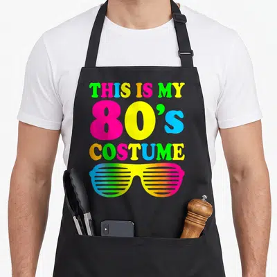 Costume outfit 80s apron - Neon stacked text reading THIS IS MY 80'S COSTUME above rainbow shutter shades — shown on a black cotton canvas apron against a white background