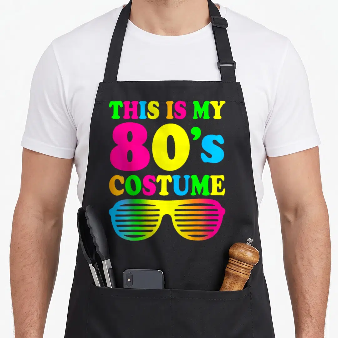 Costume outfit 80s apron - Neon stacked text reading THIS IS MY 80'S COSTUME above rainbow shutter shades — shown on a black cotton canvas apron against a white background