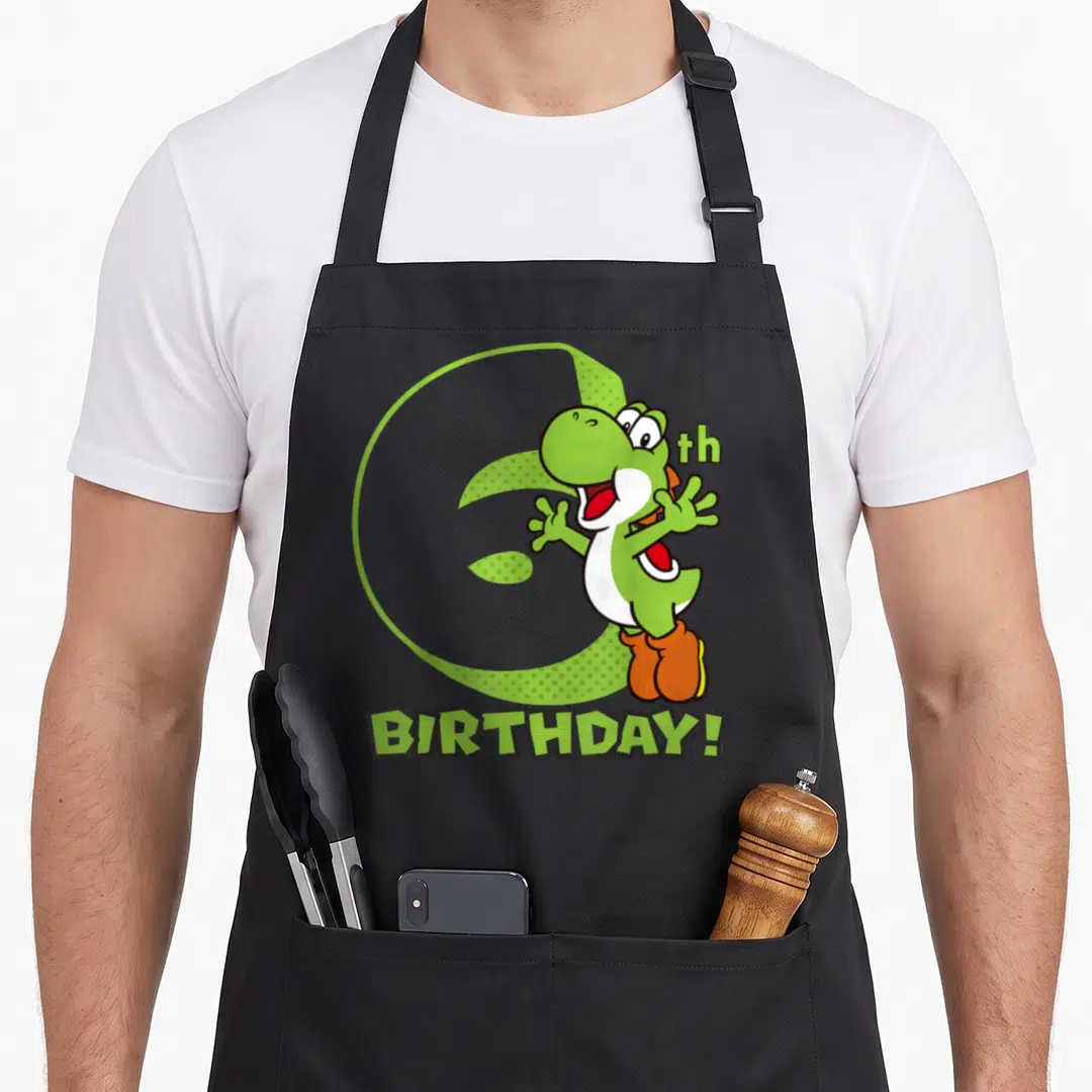 6th holiday apron - Green dinosaur overlapping large number 6 with BIRTHDAY text — shown on a black cotton canvas apron against a white background
