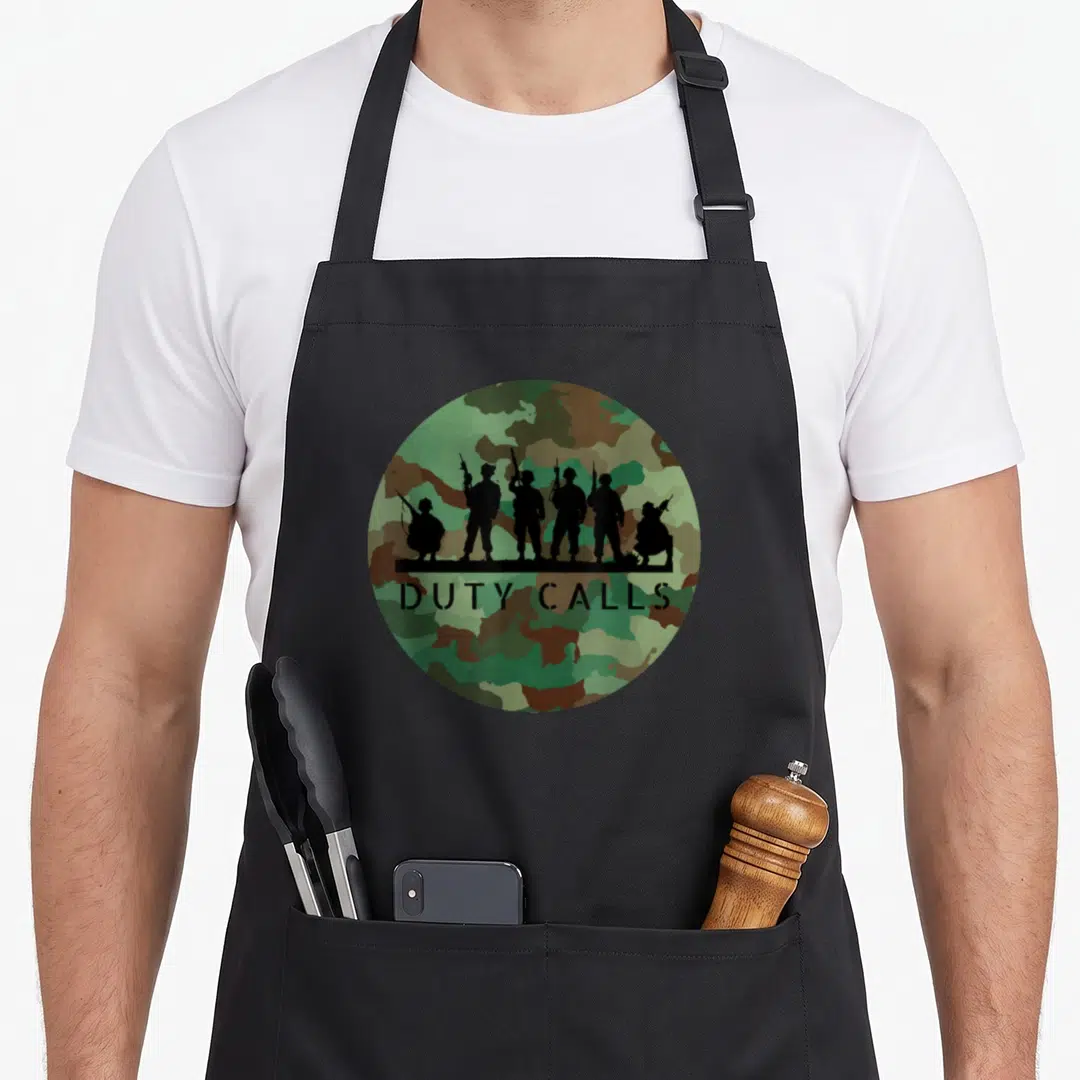 Duty camouflage apron - Six soldier silhouettes and DUTY CALLS text on green brown black camo circle — shown on a black cotton canvas apron against a white background