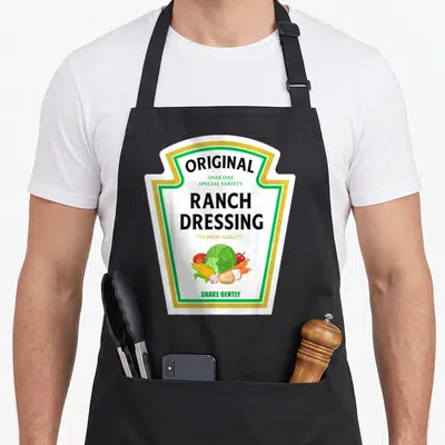 Dressing halloween apron - Ranch dressing label design with vegetables and green gold border on black apron — shown on a black cotton canvas apron against a white background