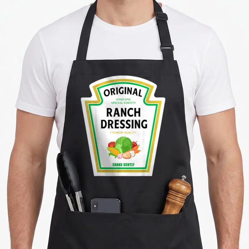 Dressing halloween apron - Ranch dressing label design with vegetables and green gold border on black apron — shown on a black cotton canvas apron against a white background