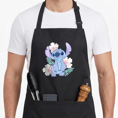 Face hawaiian apron - Blue cartoon character Stitch surrounded by white hibiscus flowers and teal leaves — shown on a black cotton canvas apron against a white background